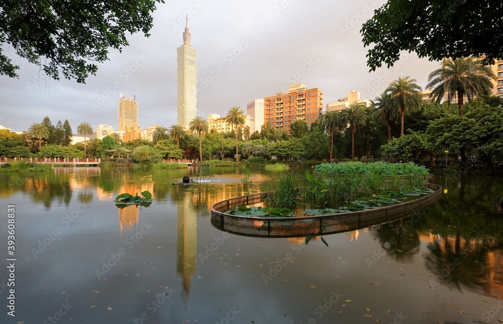 Beautiful lakeside scenery of Taipei 101 Tower among skyscrapers after an thundershower with a rainbow in the sky & reflections on the pond in an urban park in Xinyi Financial District Downtown