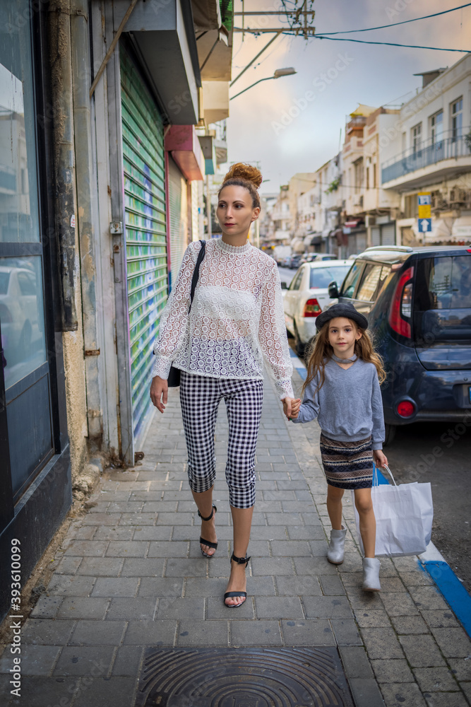 Stylish woman and a girl - mother and a daughter walk down the street and holding hands in Tel-Aviv, Israel.