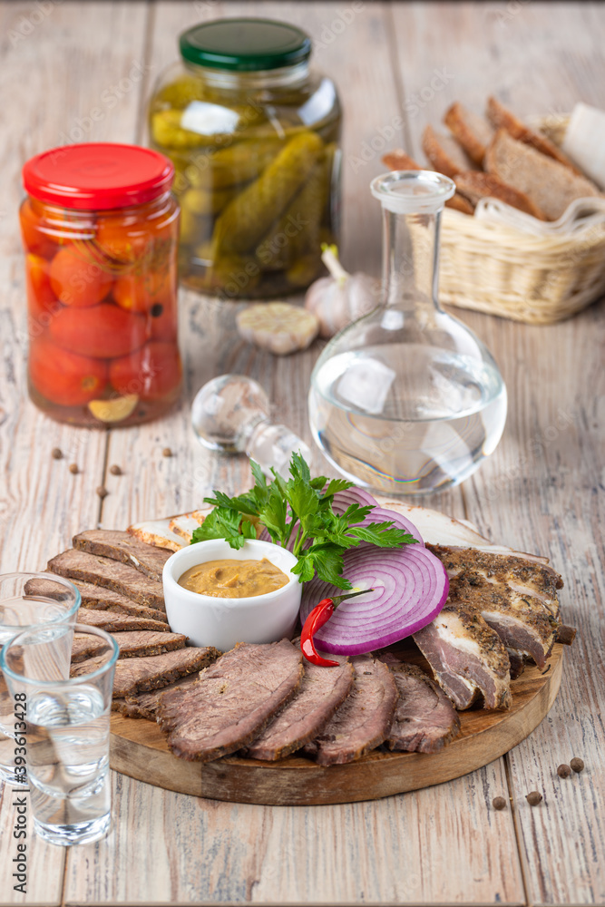 plate with cold cuts with pickles in jars and shot of vodka on wooden background, close view 