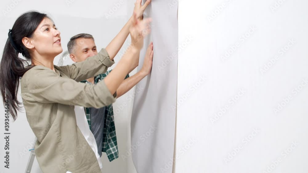 Young happy couple applying roll of wallpaper to wall smiling and discussing renovation details in new home Young happy couple applying roll of wallpaper to wall smiling and discussing renovation details in new home