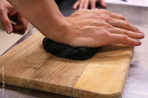 Male hands roll out the dough on a wooden board. The dough is black.