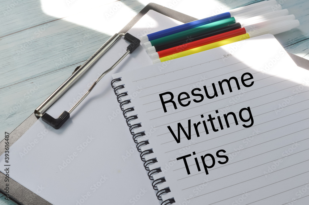 Top angle view of pen colors, paper holding file and notebook written with text RESUME WRITING TIPS on a wooden background. Business and education concept. Top angle view of pen colors, paper holding file and notebook written with text RESUME WRITING TIPS on a wooden background. Business and education concept.