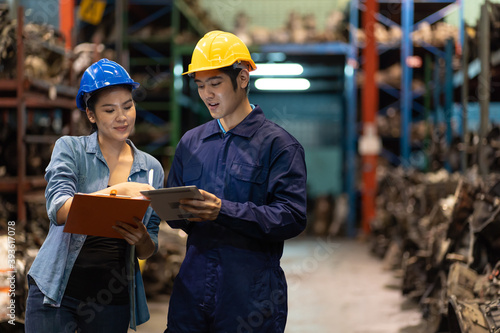 Group of Asian male and female worker in safety vest and helmet working with clipboard and checking old automotive spare parts for repair or maintenance in automotive spare parts storage warehouse