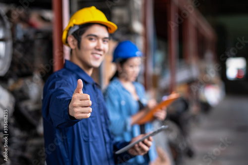 Confident Asia engineer man worker holding tablet and thumb up in the automotive spare parts warehouse with blurred background. Stock management and investigation concept. Selective focus on hand