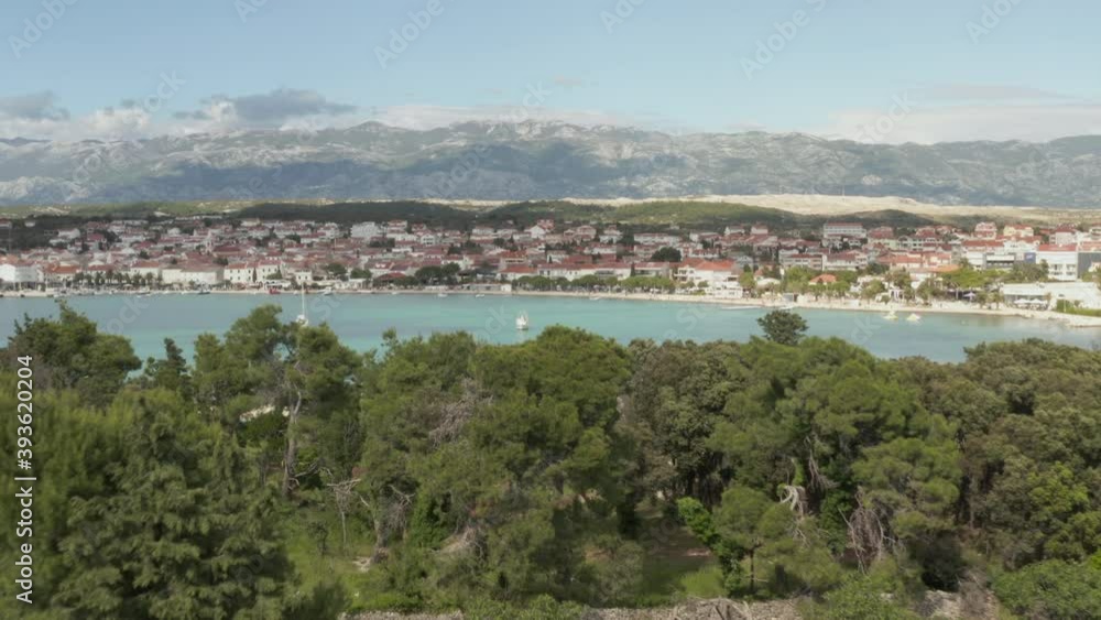 AERIAL: Flight over trees to reveal beautiful turquoise blue ocean, land in Novalja, Croatia Nature with houses and blue sky and sun AERIAL: Flight over trees to reveal beautiful turquoise blue ocean, land in Novalja, Croatia Nature with houses and blue sky and sun