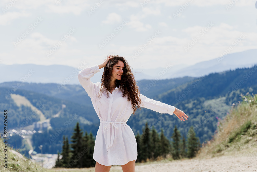 Girl traveler is smiling in the mountains. Attractive woman posing on the green hills background. Advert for travel agency. Tourism Girl traveler is smiling in the mountains. Attractive woman posing on the green hills background. Advert for travel agency. Tourism