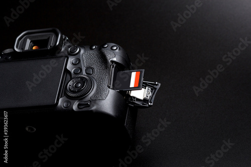 Fotografi DSLR camera body and memory card in slot on black background