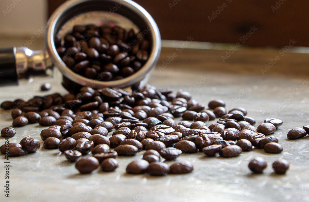 brown arabica coffee beans scattered on a concrete table with a soft focus on the filter holder. Selective focus on middle ground brown arabica coffee beans scattered on a concrete table with a soft focus on the filter holder. Selective focus on middle ground
