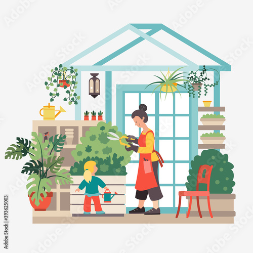 A young woman  with a little daughter waters flowers in a home greenhouse