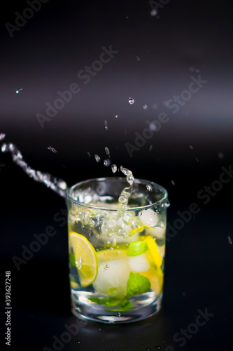 In a glass of water, ice cubes, a sprig of mint and a slice of lemon. Water splashes from the dishes are visible.