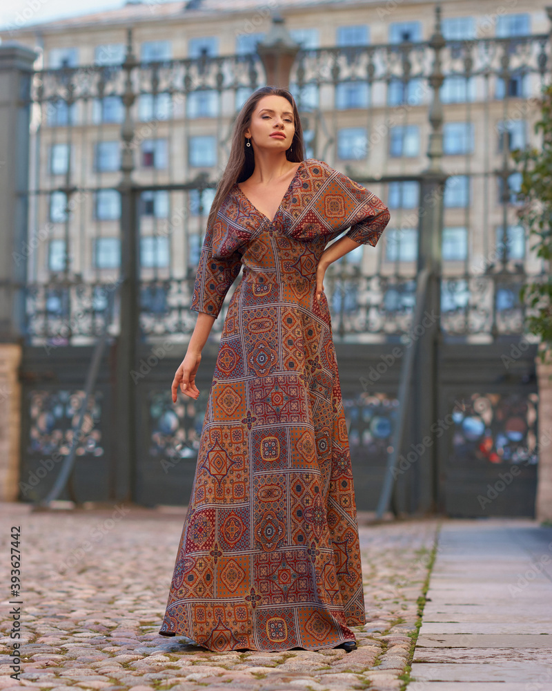 Elegant woman with longhair in brown dress walking at street in the city on a summer day