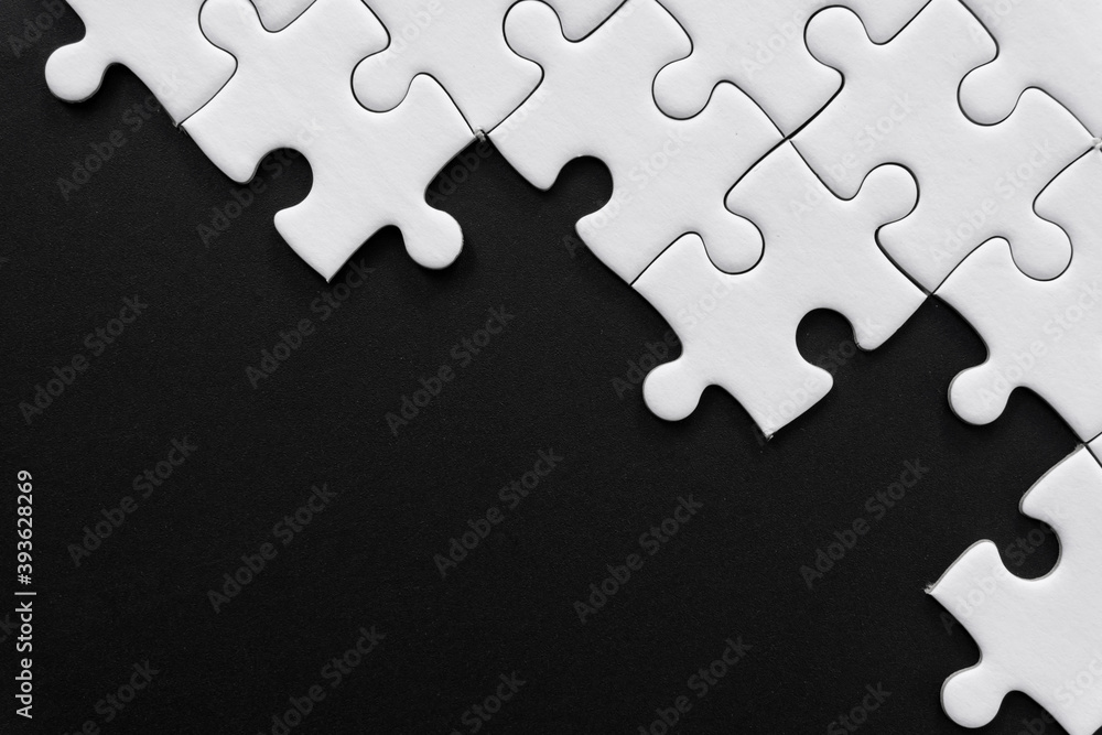 Obraz premium Unfinished white jigsaw puzzle pieces on black background with copy space