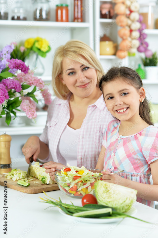 Cute little girl with her mother cooking together at kitchen table Cute little girl with her mother cooking together at kitchen table