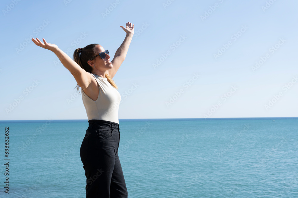Close-up portrait of smiling young woman celebrating with open arms on ocean summer background.People success , freedom and success lifestyle concept.Copy space for text. Close-up portrait of smiling young woman celebrating with open arms on ocean summer background.People success , freedom and success lifestyle concept.Copy space for text.
