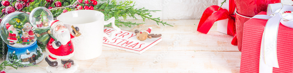 Naklejka premium Christmas greeting cad background with decor, baubles, Xmas Gift Boxes, snow globe, hot chocolate cup. White wooden Cozy Festive Winter Christmas Background. Xmas or New Year Composition.
