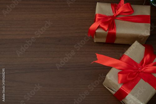 Two gifts wrapped in craft paper with a red wide ribbon stand on a wooden table with a black background. Holidays.