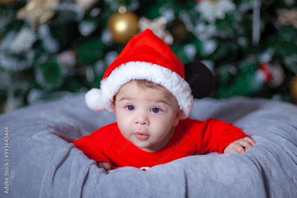 Cute baby wearing Santa suit near Christmas tree Cute baby wearing Santa suit near Christmas tree