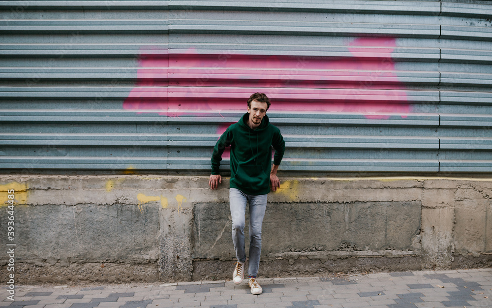 City portrait of charismatic hipster guy wearing green (watercolor) blank hoodie with space for your logo or design. Mockup for print City portrait of charismatic hipster guy wearing green (watercolor) blank hoodie with space for your logo or design. Mockup for print