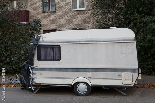 An old white trailer house caravan is in a street parking lot among apartment buildings.