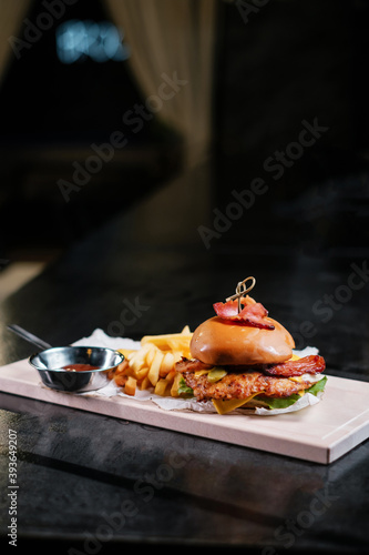 Juicy burger with fries on wooden board.