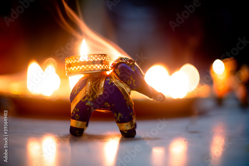 small elephant incense holder with smoke coming out and an out fo focus background with diya oil lamps lit behind it with flickering flames