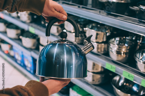 A man in a supermarket holds a metal kettle.