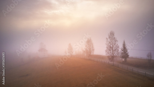 Obraz na płótnie Morning fog in mountain valley. Forest covered by low clouds. Alpine village. Autumn rural landscape. Cold November morning. w salonie