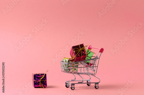 shopping trolley full of present boxes copy space, shopping concept poster on a pink background