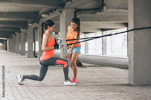 Two young female work out on trx suspension trainer.Outdoor workout.  