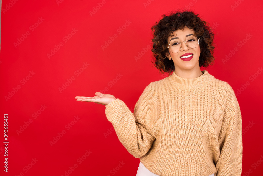 Positive glad Young beautiful Arab woman wearing beige sweater, says: wow how exciting it is, has amazed expression, shows something on blank space with open hand. Advertisement concept. Positive glad Young beautiful Arab woman wearing beige sweater, says: wow how exciting it is, has amazed expression, shows something on blank space with open hand. Advertisement concept.