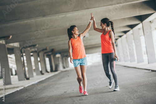 Two young woman giving high five to each other.They relaxing after jogging on street. 