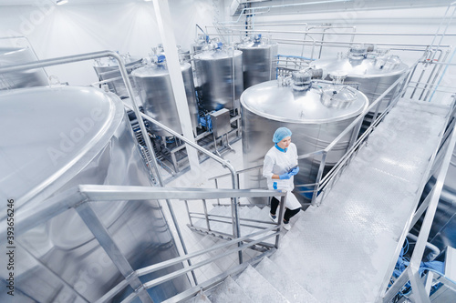 Female worker operator in uniform holding computer tablet near food factory production line