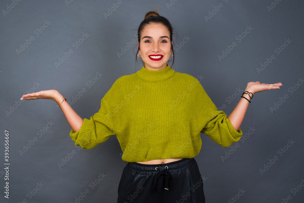 Cheerful cheery optimistic Young beautiful hispanic woman wearing green sweater against gray background holding two palms copy space Cheerful cheery optimistic Young beautiful hispanic woman wearing green sweater against gray background holding two palms copy space