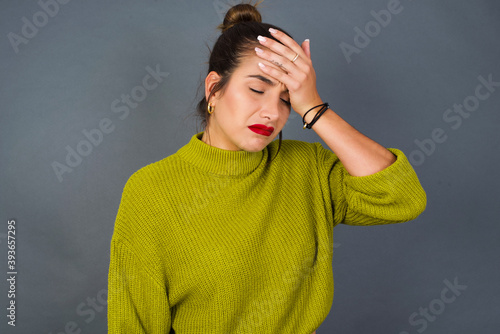 A very upset and lonely Young beautiful hispanic woman wearing green sweater against gray background crying,