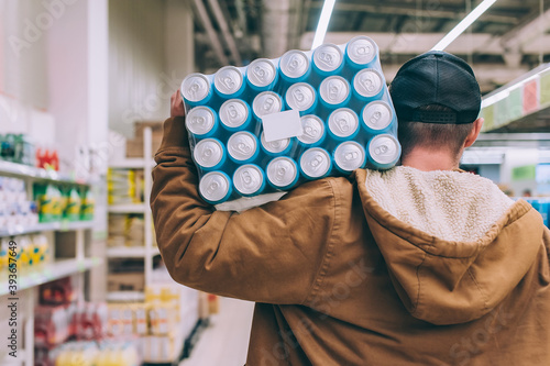 A shopper in a supermarket holds a package of beer in his hands.
