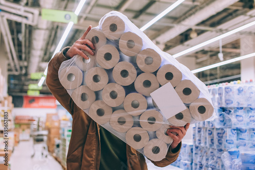 A shopper in a supermarket holds a package of toilet paper.