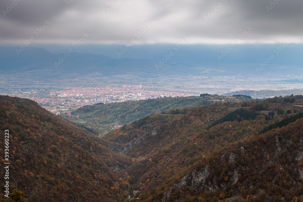 Dark, moody, murky sky above distant Pirot city, foreground canyon and autumn, golden colored trees