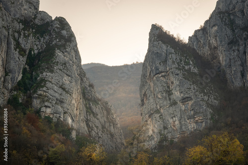 Close up of impressive pointy mountain cliffs at the misty entrance of Jerma river canyon with foreground autumn colored trees
