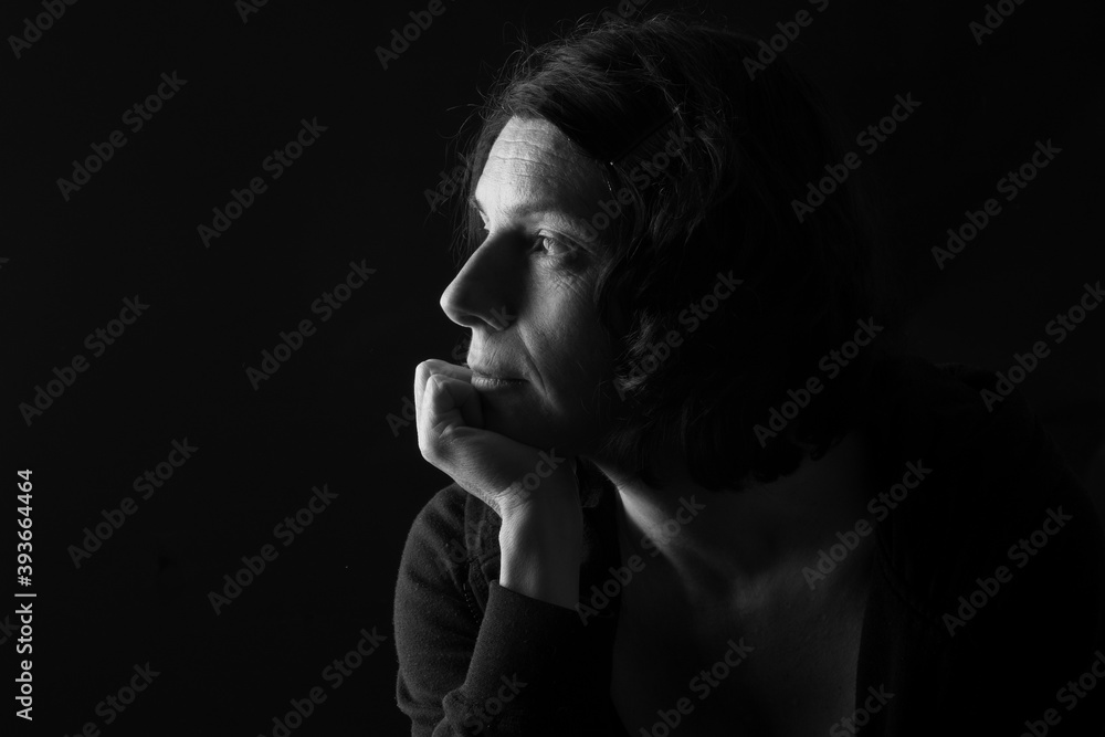 low key portrait of serious woman with hand on chin and thinking on black background low key portrait of serious woman with hand on chin and thinking on black background