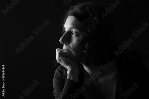 low key portrait of serious woman with hand on chin and thinking on black background