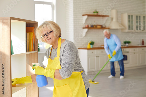 Happy senior couple woman and man in aprons and gloves making cleaning at home