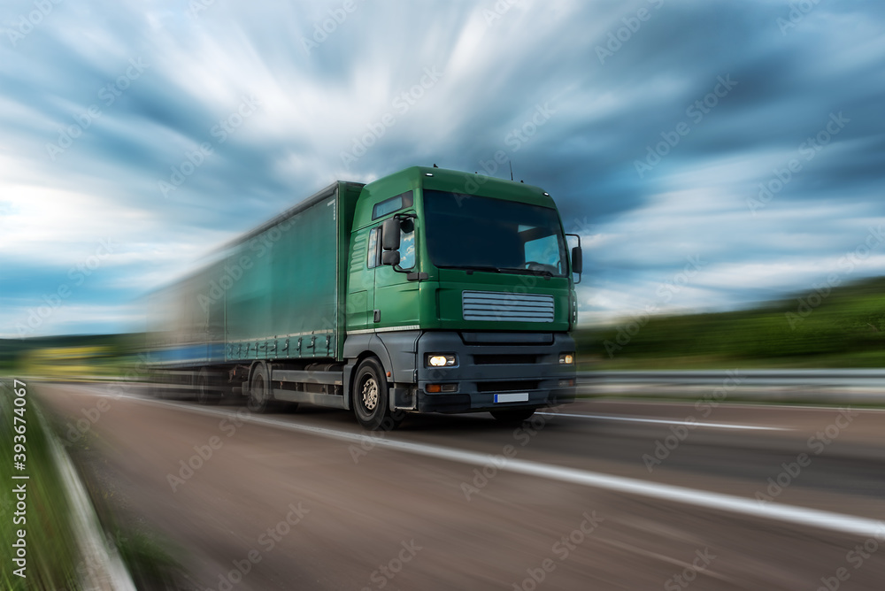 Green Lorry truck speeding on freeway at sunset, motion blurred.