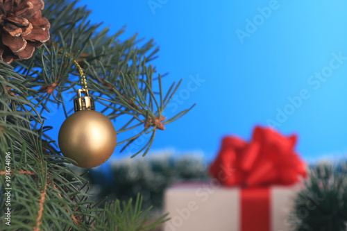 New year's gift under the branches of the tree. White gift box with red ribbon and red bow on a blue background. With space for text.