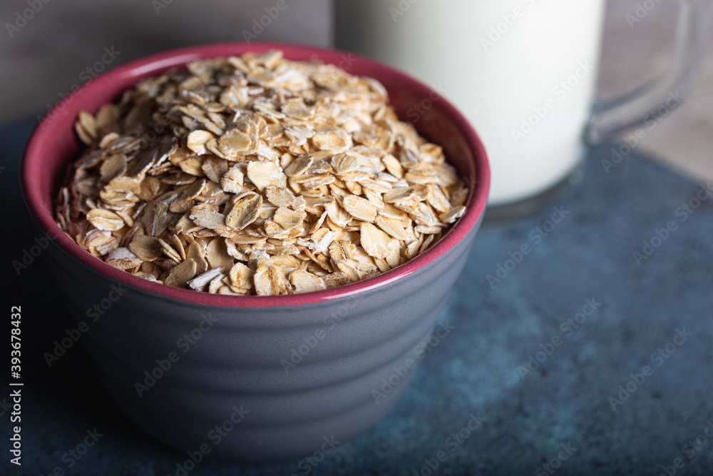 Dry rolled oatmeal in a bowl with milk on dark blue background. Healthy cereal flakes in a ceramic bowl and glass of milk close-up. Dry rolled oatmeal in a bowl with milk on dark blue background. Healthy cereal flakes in a ceramic bowl and glass of milk close-up.
