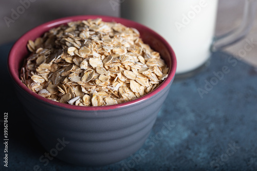 Dry rolled oatmeal in a bowl with milk on dark blue background. Healthy cereal flakes in a ceramic bowl and glass of milk close-up.
