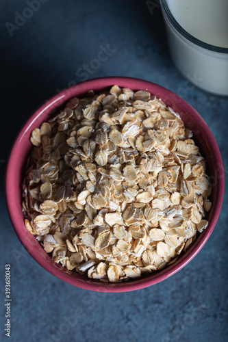 Dry rolled oatmeal in a bowl with milk on dark blue background. Healthy cereal flakes in a ceramic bowl and glass of milk close-up. Top view.