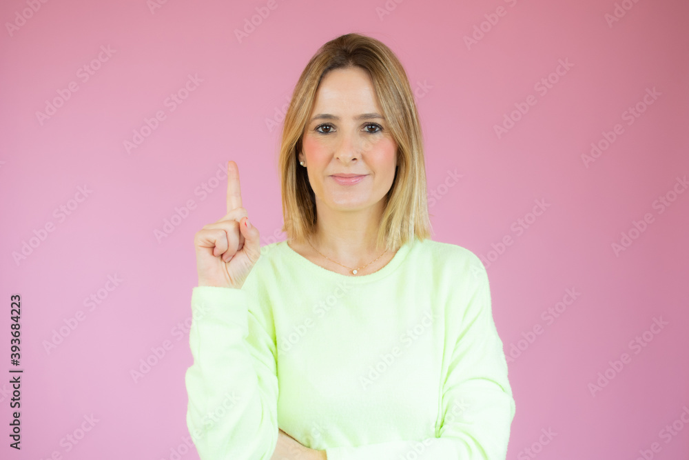 Portrait of a happy young woman dressed in casual sweater pointing finger up at copy space isolated over pink background Portrait of a happy young woman dressed in casual sweater pointing finger up at copy space isolated over pink background