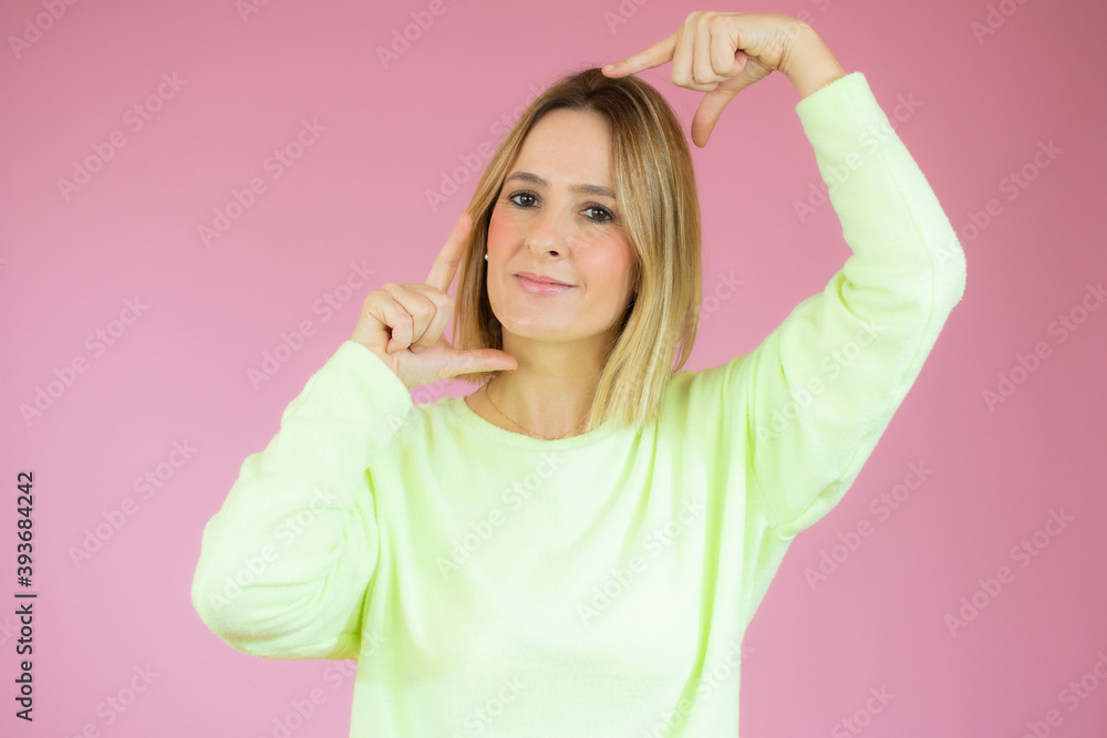 Young beautiful blonde woman wearing casual sweater over pink background smiling making frame with hands and fingers with happy face. Creativity and photography concept. Young beautiful blonde woman wearing casual sweater over pink background smiling making frame with hands and fingers with happy face. Creativity and photography concept.