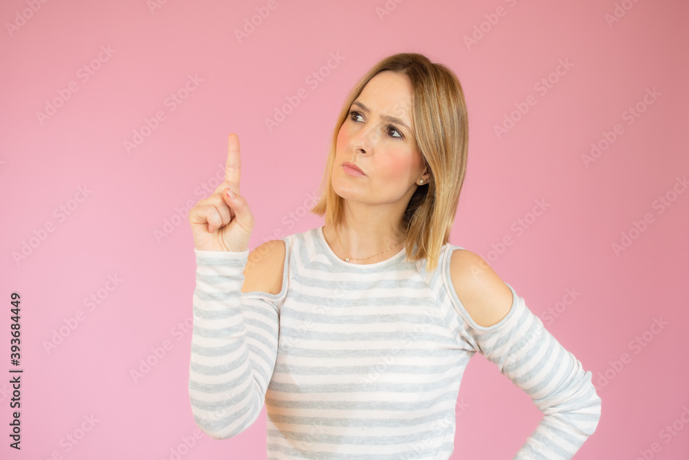 Portrait of a happy young woman dressed in casual t-shirt pointing finger up at copy space isolated over pink background Portrait of a happy young woman dressed in casual t-shirt pointing finger up at copy space isolated over pink background