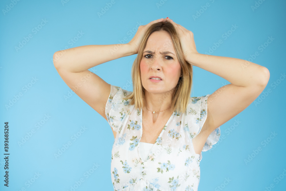 Portrait of young woman with blond hair touching her head and expressing worry isolated over blue background Portrait of young woman with blond hair touching her head and expressing worry isolated over blue background